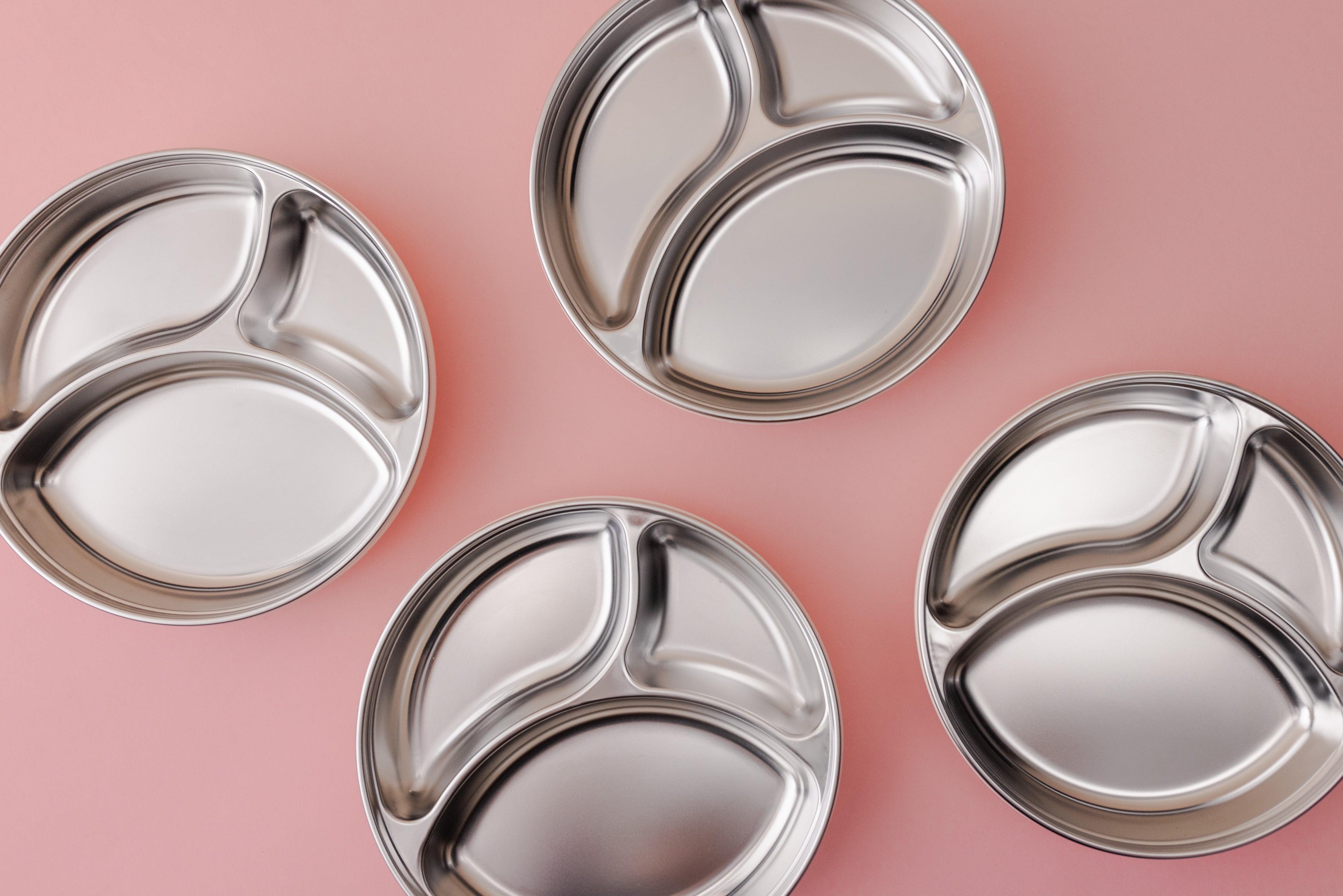 A top down view of 4 stainless steel suction plates on a pink background.